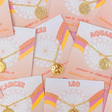 Collection of zodiac-themed jewelry cards with gold necklaces on a matching card background.