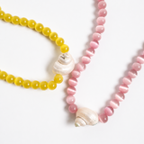 Two beaded necklaces, one yellow and one pink, with shell accents on a white background.