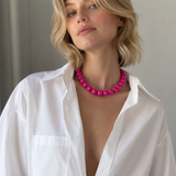 Woman wearing a bright pink necklace with an open white shirt against a neutral background