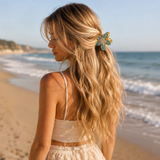 a model ong wavy blond hair on the beach, wearing flower shape hair claw for half of hair to hold on the back