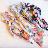 Trio of scarf hair scrunchies with colorful blooming floral patterns and soft, flowing ribbons—ideal for adding a lively, festival-ready touch to any look.