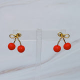 Playful gold-tone earrings featuring a bow and cherry design, adding a whimsical and charming touch to your style.