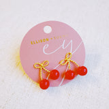 Playful gold-tone earrings featuring a bow and cherry design, adding a whimsical and charming touch to your style.