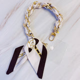 Stylish braided scarf lanyard featuring a gold-tone chain intertwined with patterned fabric, designed to securely attach to a phone while doubling as a chic fashion accessory.