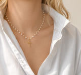 Pearl necklace with a gold cross pendant worn by a person in a white shirt.