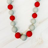 Necklace with red and gray beads on a white wooden surface