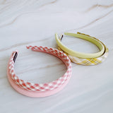 A set of padded fabric headbands in assorted pastel and plaid designs, including soft pink, green tones. Each headband features a cushioned, textured surface that blends solid and patterned fabrics for a stylish, comfortable everyday accessory.