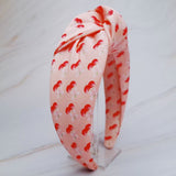 Soft satin headband adorned with a playful cherry and bow pattern, featuring vibrant red cherries and delicate bows on a pink background.