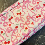 Rectangular cosmetic case featuring an all-over cherry and bow print with a top handle, perfect for everyday storage of beauty essentials.