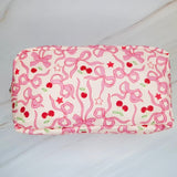Rectangular cosmetic case featuring an all-over cherry and bow print with a top handle, perfect for everyday storage of beauty essentials.