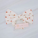 Playful hair scrunchie featuring a charming red cherry print and an attached bow tie, perfect for adding a sweet and fruity flair to ponytails or buns.