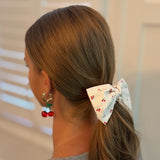 Playful hair scrunchie featuring a charming red cherry print and an attached bow tie, perfect for adding a sweet and fruity flair to ponytails or buns.