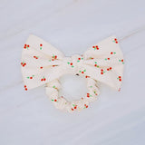 Playful hair scrunchie featuring a charming red cherry print and an attached bow tie, perfect for adding a sweet and fruity flair to ponytails or buns.