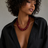 Woman wearing a red beaded necklace with a black shirt against a neutral background