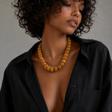 Woman wearing a black shirt and amber necklace against a gray background
