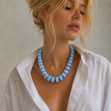 Woman wearing a blue beaded necklace with a plain background