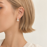 Pearl earring worn by a person with short blonde hair on a neutral background