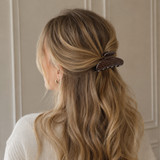 Woman with wavy hair wearing a decorative hair clip against a neutral background