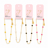 Four gold anklets with different colored beads on pink cards with 'ey' branding.