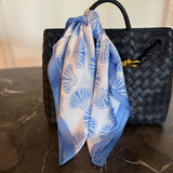 Blue and white patterned scarf draped over a black woven handbag on a marble surface.