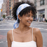 Woman wearing a white tank top and blue headscarf on a city street