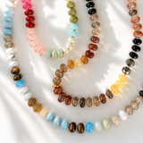 A set of five multi-colored beaded gemstone necklaces arranged in overlapping loops on a white fabric background with soft shadows.