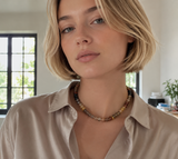 Woman wearing a beige shirt and a beaded necklace indoors