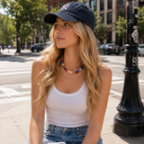 A woman wearing Colorful irregular shapes of beads in a necklace and a ball cap on the street