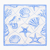 Napkin with blue sea-themed design featuring mermaid, shells, and starfish on a white background. Square scarf featuring a blue and white coastal print with seashells, starfish, and ocean-inspired illustrations, designed for styling around the neck, hair, or tied to a handbag.