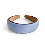 A softly padded wide headband in a solid hue, finished with a distinct contrast border trim along the edges, offering a chic and polished look for everyday wear.