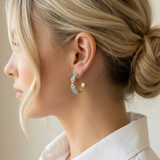 Close-up of a woman wearing gold and blue hoop earrings with a neutral background