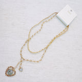 Layered gold-tone necklace featuring dual chain links and a vintage-inspired heart pendant centerpiece—offering a romantic, bold accent perfect for elevating any look.