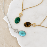 Equestrian bit design with colored natural stone oval pendant, 3 different necklaces on the marble board.