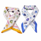 Two colorful scarves with sea-themed patterns on a white background. Square scarf in butter yellow featuring sea shells, starfish, and ocean-inspired motifs with a contrasting border, designed for styling around the neck, hair, or handbag.