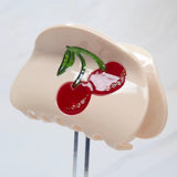 Playful cherry-themed hair claw clip featuring bright red cherries and green stems, adding a sweet and fruity flair to any hairstyle.