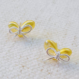Delicate gold heart-shaped stud earrings adorned with a silver bow accent—perfect for adding a touch of charm and elegance to any look.