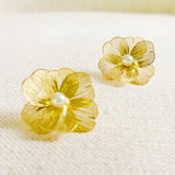 Gold flower-shaped earrings with pearl centers on a textured surface