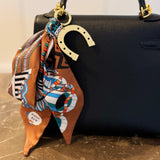 Chic bag charm featuring a flowing printed scarf tied to a gold-tone chain with assorted golden charms for a luxe, fashion-forward accessory