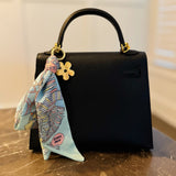 Chic bag charm featuring a flowing printed scarf tied to a gold-tone chain with assorted golden charms for a luxe, fashion-forward accessory
