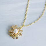 Gold-tone necklace featuring a daisy-inspired pendant with a luminous pearl center surrounded by sparkling crystal-studded petals. The design blends classic elegance with a fresh, feminine touch, perfect for layering or wearing solo.