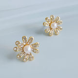Gold-tone floral stud earrings featuring a luminous pearl center surrounded by petal-shaped sections adorned with sparkling crystals. The earrings create a radiant, feminine look that blends timeless charm with elegant shine.