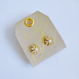 Gold-tone floral stud earrings featuring a luminous pearl center surrounded by petal-shaped sections adorned with sparkling crystals. The earrings create a radiant, feminine look that blends timeless charm with elegant shine.
