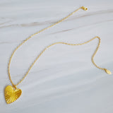 Close-up of a gold-tone heart-shaped pendant necklace engraved with the word “MAMA.” The pendant features radiant sunburst detailing and a polished finish, creating a luminous and heartfelt design that symbolizes warmth and love