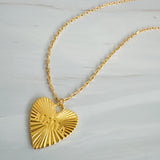 Close-up of a gold-tone heart-shaped pendant necklace engraved with the word “MAMA.” The pendant features radiant sunburst detailing and a polished finish, creating a luminous and heartfelt design that symbolizes warmth and love
