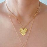 Close-up of a gold-tone heart-shaped pendant necklace engraved with the word “MAMA.” The pendant features radiant sunburst detailing and a polished finish, creating a luminous and heartfelt design that symbolizes warmth and love