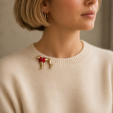A close-up of a woman wearing a gold-tone dog-shaped brooch with a red heart on a cream knit sweater.
