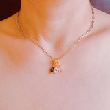 Close-up of a gold paperclip chain necklace featuring an eclectic mix of dangling gem-shaped charms in various cuts and colors, the stones clustered at the center.