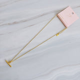 A polished gold chain necklace featuring a T-bar pendant drop at the center. The design highlights a modern, structured silhouette with timeless charm and a subtle statement finish
