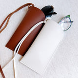 Glass case bag charm with an open-top design and strap attachment, perfect for hanging on your bag to hold glasses or other small essentials in style.
