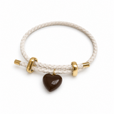 A braided white cord bracelet with gold-toned metal sliders and a dark brown heart-shaped charm featuring a white wing design, shown on a clean white background.